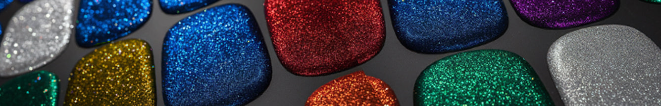 Close-up of various vibrant metal flake paint finishes in red, blue, green, and silver, sparkling with metallic flakes of different sizes and shapes, displayed on a dark surface to highlight their shimmering and reflective qualities.